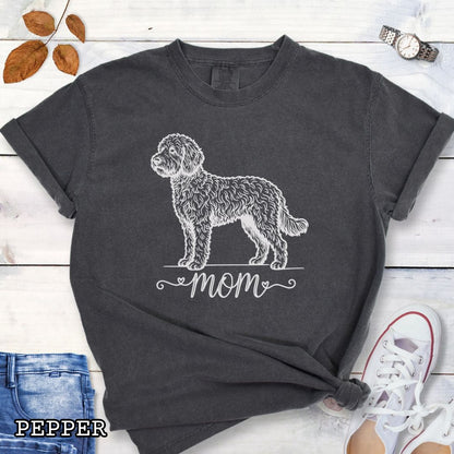 Dark grey Comfort Colors t-shirt for Doodle dog moms with a vintage-style Doodle dog illustration and 'mom' text in script lettering beneath it, shown on a wooden surface with jeans and shoes.