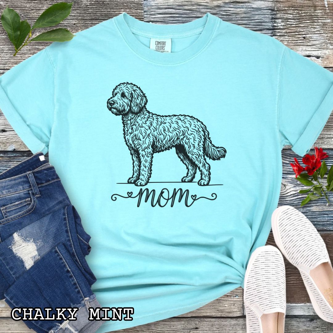 Mint Comfort Colors t-shirt for Doodle dog moms with a vintage-style Doodle dog illustration and 'mom' text in script lettering beneath it, shown on a wooden surface with jeans and shoes.