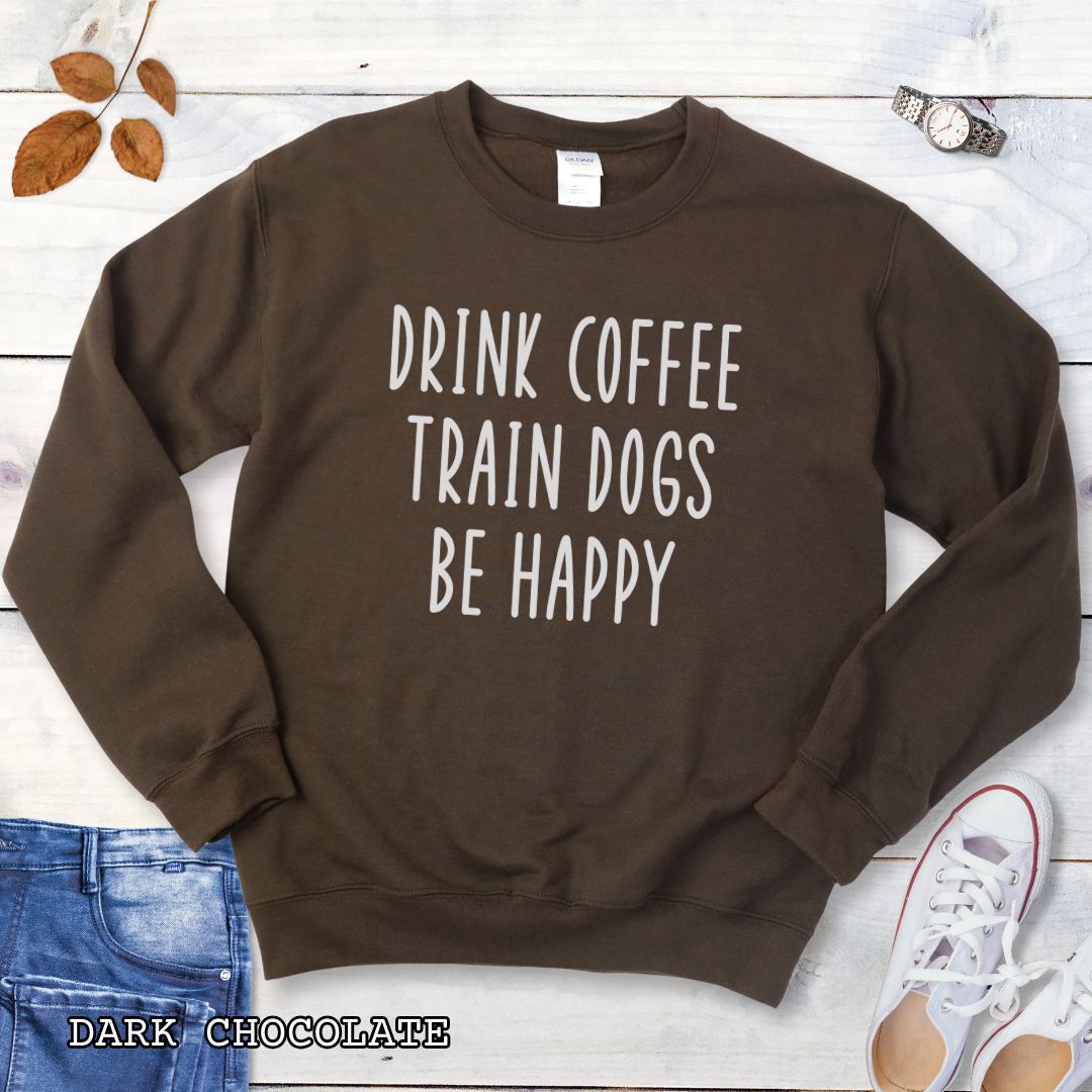 Chocolate brown unisex dog training sweatshirt with 'Drink Coffee Train Dogs Be Happy' text on a wooden surface with jeans and shoes.