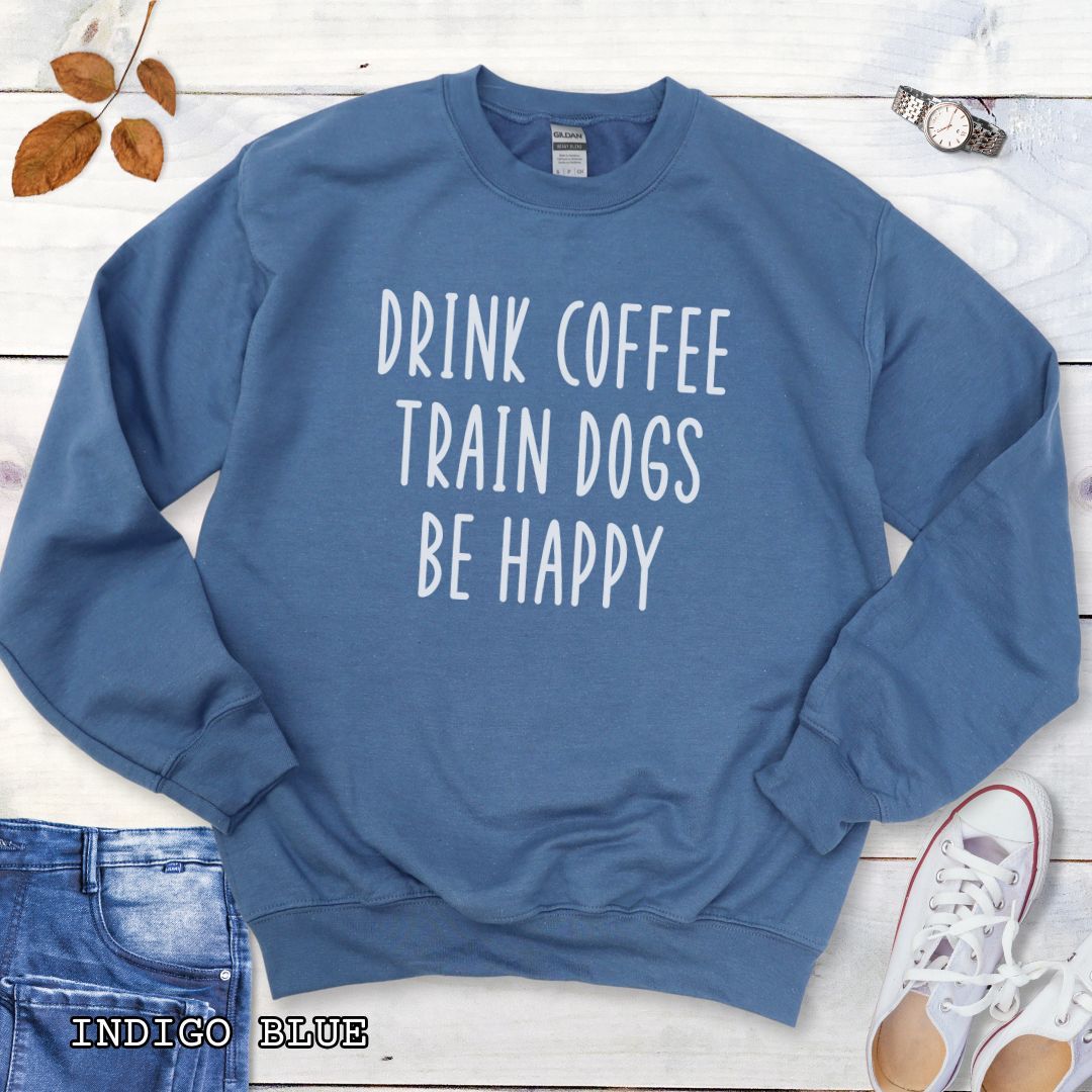 Blue unisex dog training sweatshirt with 'Drink Coffee Train Dogs Be Happy' text on a wooden surface with jeans and shoes.