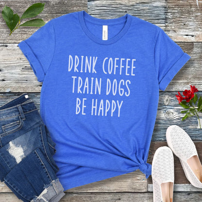 Royal blue unisex dog training t-shirt with 'Drink Coffee Train Dogs Be Happy' text on a wooden surface with jeans and shoes.