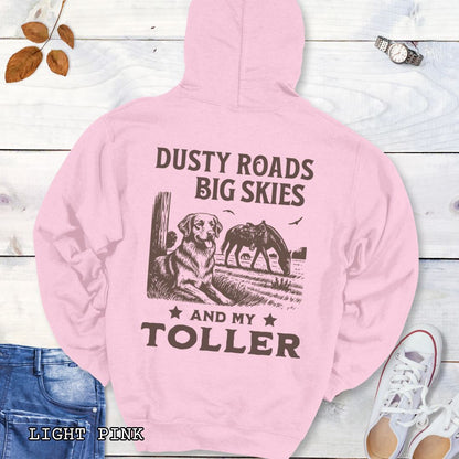 Back view of a light pink hoodie featuring a Western-style design with grazing horse, rustic fence, and a Duck Tolling Retriever illustration; text reads “Dusty Roads, Big Skies, and My Toller.”