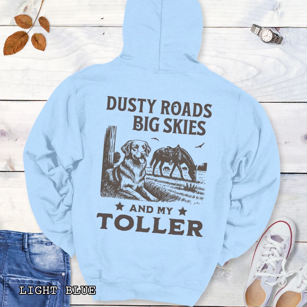 Back view of a light blue hoodie featuring a Western-style design with grazing horse, rustic fence, and a Duck Tolling Retriever illustration; text reads “Dusty Roads, Big Skies, and My Toller.”