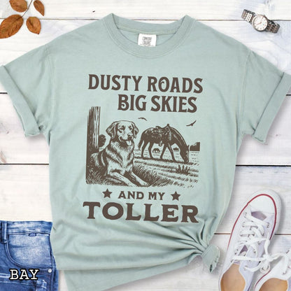 Light green Comfort Colors t-shirt featuring a Western-style design with grazing horse, rustic fence, and a Duck Tolling Retriever illustration; text reads “Dusty Roads, Big Skies, and My Toller.”