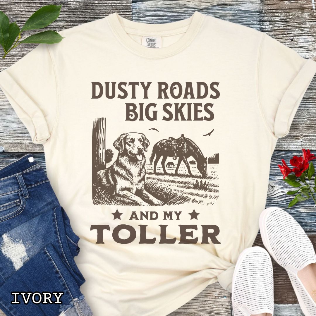 Ivory Comfort Colors t-shirt featuring a Western-style design with grazing horse, rustic fence, and a Duck Tolling Retriever illustration; text reads “Dusty Roads, Big Skies, and My Toller.”