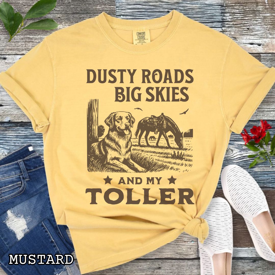 Mustard-yellow Comfort Colors t-shirt featuring a Western-style design with grazing horse, rustic fence, and a Duck Tolling Retriever illustration; text reads “Dusty Roads, Big Skies, and My Toller.”