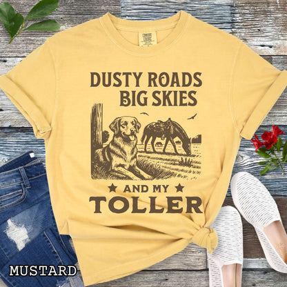 Mustard-yellow Comfort Colors t-shirt featuring a Western-style design with grazing horse, rustic fence, and a Duck Tolling Retriever illustration; text reads “Dusty Roads, Big Skies, and My Toller.”