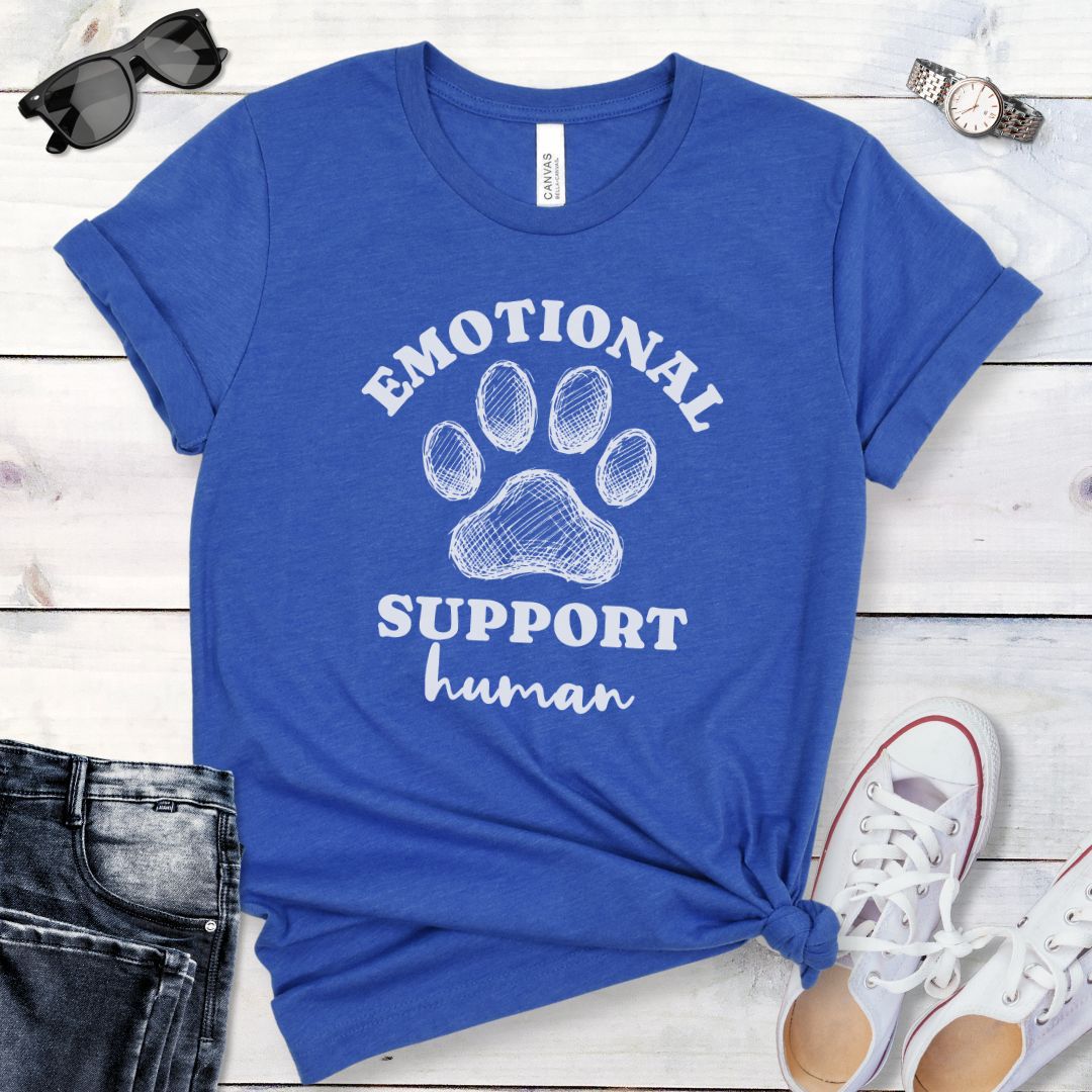 Blue unisex t-shirt for dog lovers with large paw print and humorous text 'EMOTIONAL SUPPORT human' in bold lettering, shown on a wooden surface alongside jeans and shoes.