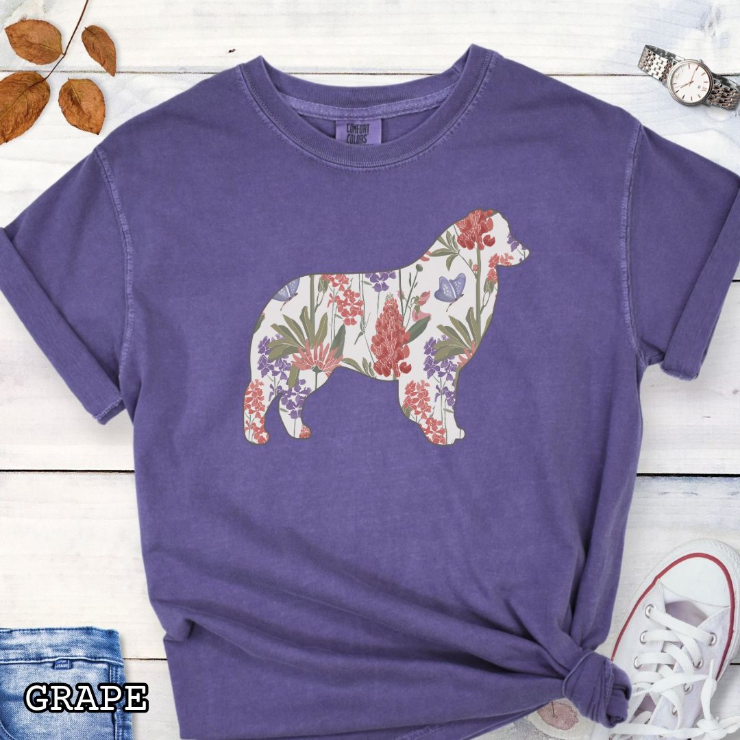 Purple Comfort Colors t-shirt with a floral-filled silhouette of an Australian Shepherd, accompanied by a pair of rolled-up blue jeans and a pair of white shoes on a wooden surface.
