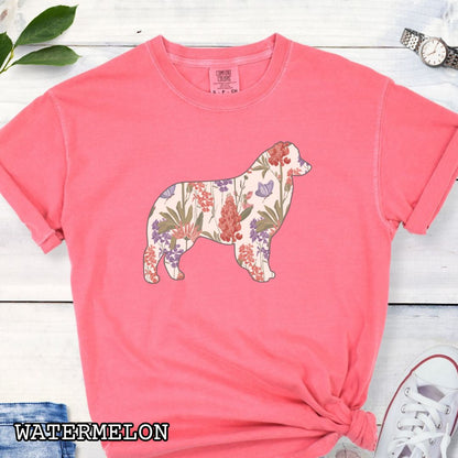 Watermelon-color Comfort Colors t-shirt with a floral-filled silhouette of an Australian Shepherd, accompanied by a pair of rolled-up blue jeans and a pair of white shoes on a wooden surface.