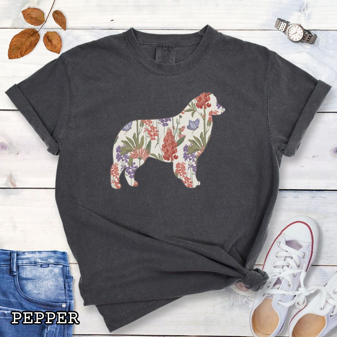 Dark grey Comfort Colors t-shirt with a floral-filled silhouette of an Australian Shepherd, accompanied by a pair of rolled-up blue jeans and a pair of white shoes on a wooden surface.