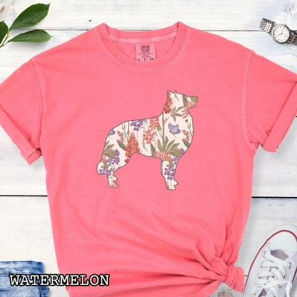 Watermelon-color Comfort Colors t-shirt with a floral-filled silhouette of a Belgian Sheepdog/Tervuren, accompanied by a pair of rolled-up blue jeans and a pair of white shoes on a wooden surface.