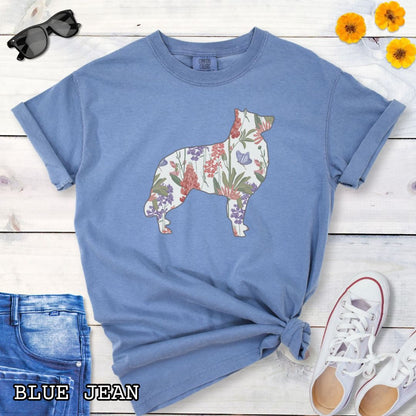 Blue Comfort Colors t-shirt with a floral-filled silhouette of a Belgian Sheepdog/Tervuren, accompanied by a pair of rolled-up blue jeans and a pair of white shoes on a wooden surface.
