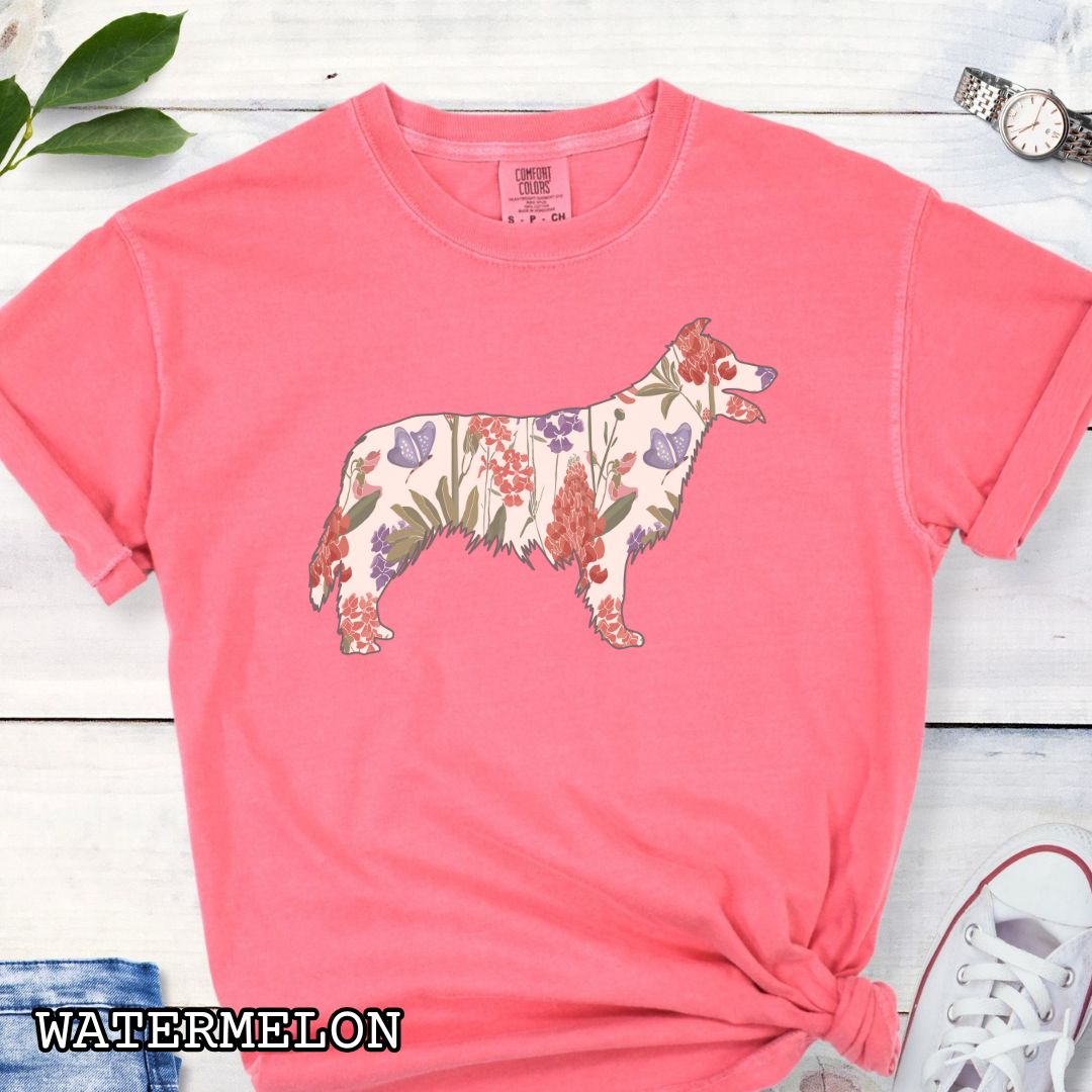 Bright pink Comfort Colors t-shirt with floral Border Collie dog design on a wooden surface with jeans and shoes.