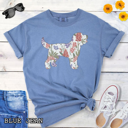Blue Comfort Colors t-shirt with a floral-filled silhouette of a Doodle dog, accompanied by a pair of rolled-up blue jeans and a pair of white shoes on a wooden surface.
