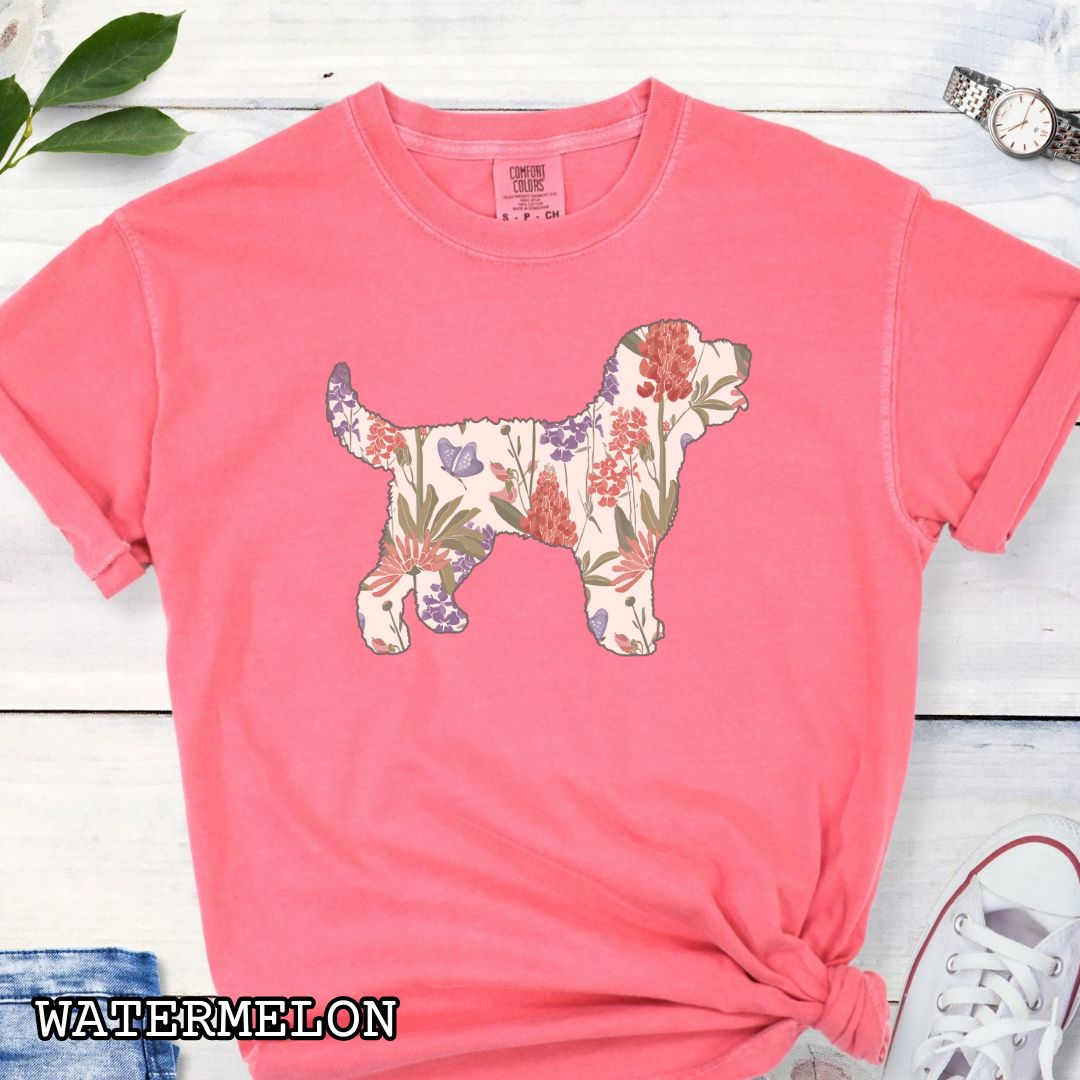 Watermelon Comfort Colors t-shirt with a floral-filled silhouette of a Doodle dog, accompanied by a pair of rolled-up blue jeans and a pair of white shoes on a wooden surface.