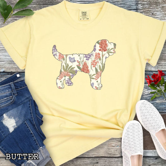 Yellow Comfort Colors t-shirt with a floral-filled silhouette of a Doodle dog, accompanied by a pair of rolled-up blue jeans and a pair of white shoes on a wooden surface.