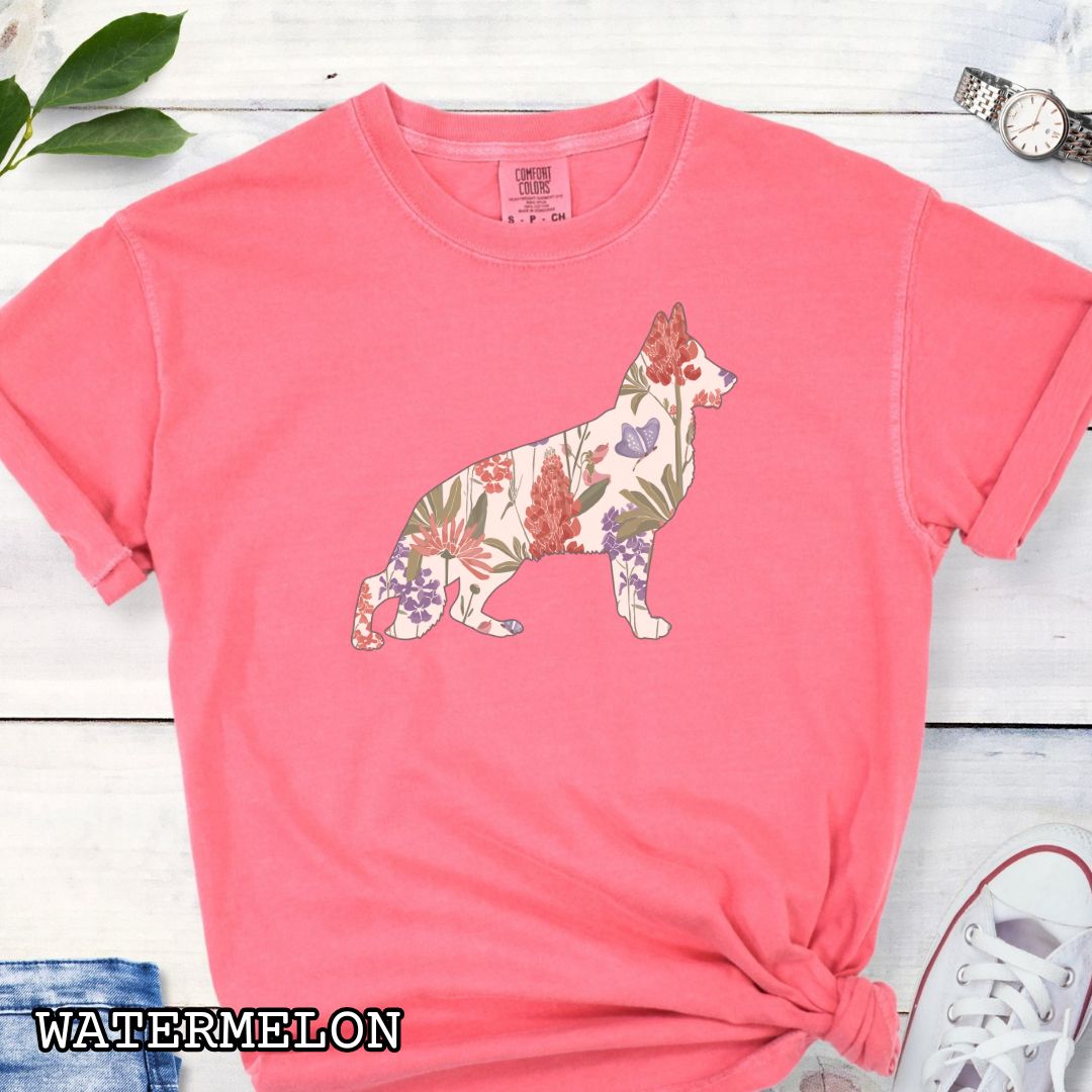 Bright Pink (Watermelon) Comfort Colors t-shirt with a floral-filled silhouette of a German Shepherd, accompanied by a pair of rolled-up blue jeans and a pair of white shoes on a wooden surface.