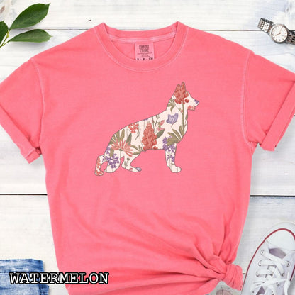 Bright Pink (Watermelon) Comfort Colors t-shirt with a floral-filled silhouette of a German Shepherd, accompanied by a pair of rolled-up blue jeans and a pair of white shoes on a wooden surface.