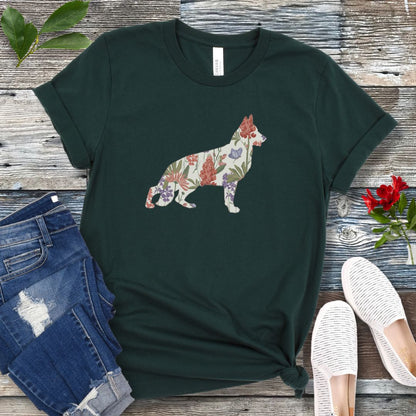 A forest green t-shirt with a floral-filled silhouette of a German Shepherd, accompanied by a pair of rolled-up blue jeans and a pair of white shoes on a wooden surface.