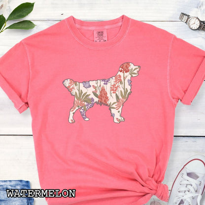 Watermelon-color Comfort Colors t-shirt with a floral-filled silhouette of a Golden Retriever, accompanied by a pair of rolled-up blue jeans and a pair of white shoes on a wooden surface.