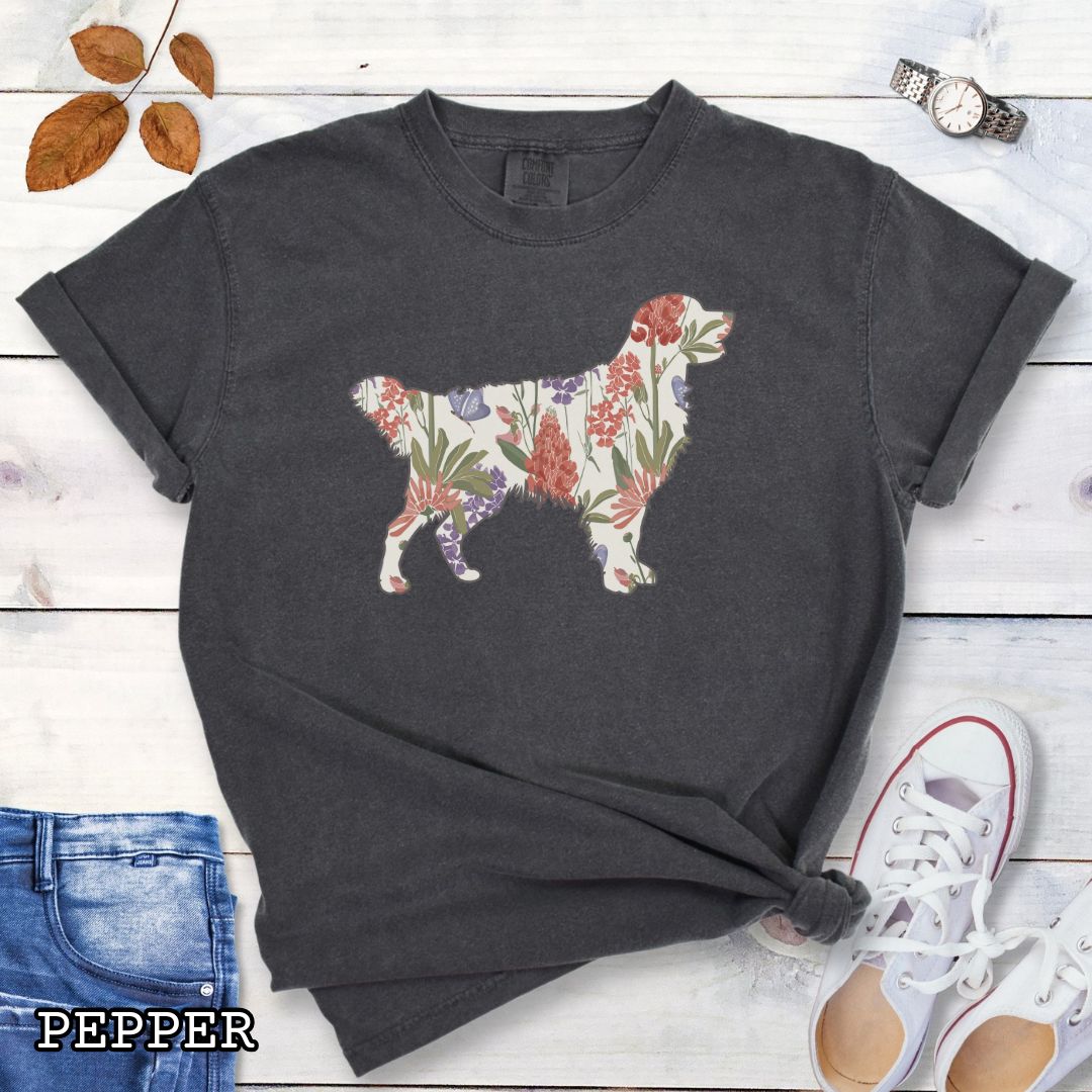 Dark grey Comfort Colors t-shirt with a floral-filled silhouette of a Golden Retriever, accompanied by a pair of rolled-up blue jeans and a pair of white shoes on a wooden surface.