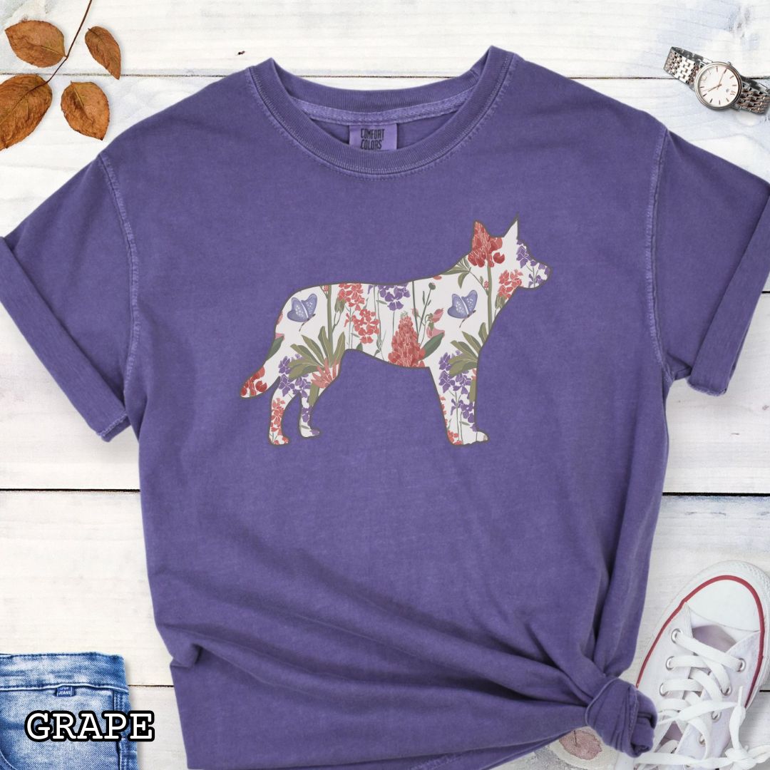 Purple Comfort Colors t-shirt with a floral-filled silhouette of a cattle dog, accompanied by a pair of rolled-up blue jeans and a pair of white shoes on a wooden surface.