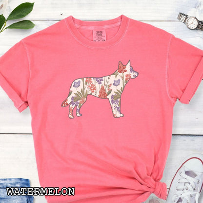 Watermelon-color Comfort Colors t-shirt with a floral-filled silhouette of a cattle dog, accompanied by a pair of rolled-up blue jeans and a pair of white shoes on a wooden surface.