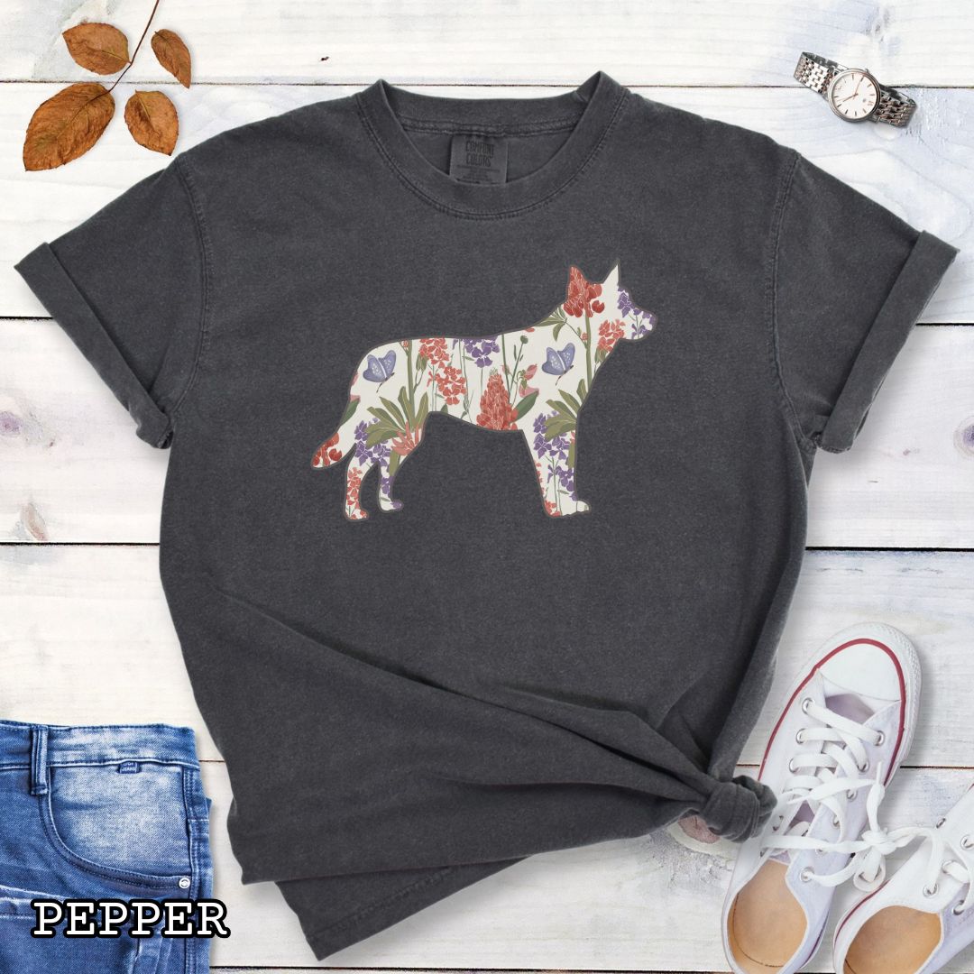 Dark grey Comfort Colors t-shirt with a floral-filled silhouette of a cattle dog, accompanied by a pair of rolled-up blue jeans and a pair of white shoes on a wooden surface.