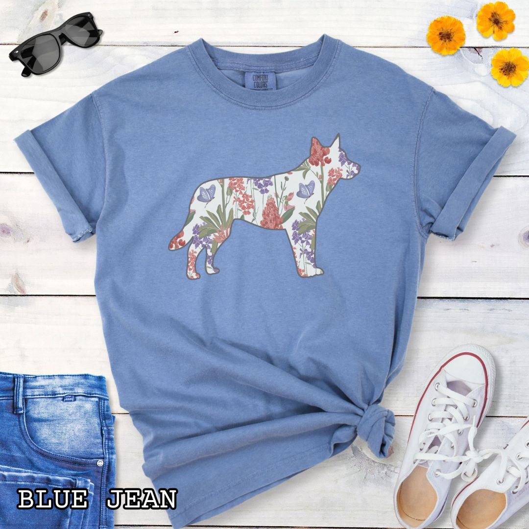 Blue Comfort Colors t-shirt with a floral-filled silhouette of a cattle dog, accompanied by a pair of rolled-up blue jeans and a pair of white shoes on a wooden surface.