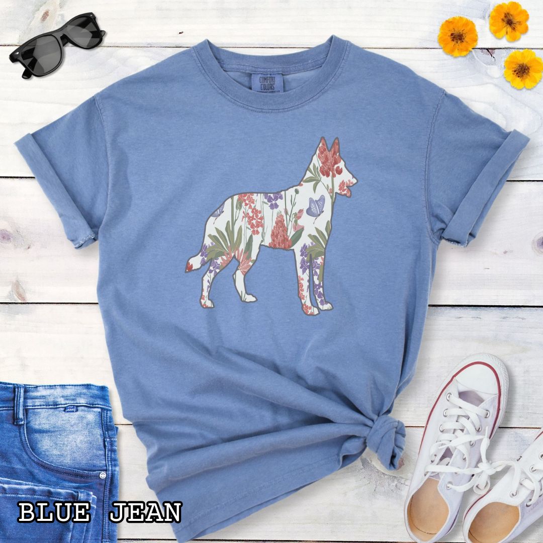 Blue Comfort Colors t-shirt with a floral-filled silhouette of a Belgian Malinois, accompanied by a pair of rolled-up blue jeans and a pair of white shoes on a wooden surface.