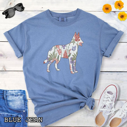 Blue Comfort Colors t-shirt with a floral-filled silhouette of a Belgian Malinois, accompanied by a pair of rolled-up blue jeans and a pair of white shoes on a wooden surface.