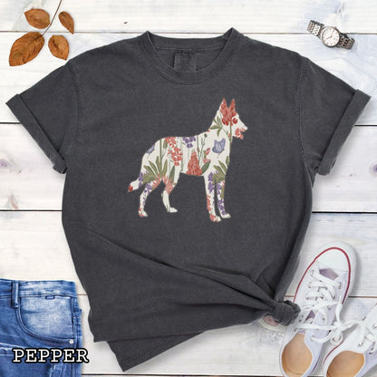 Dark grey Comfort Colors t-shirt with a floral-filled silhouette of a Belgian Malinois, accompanied by a pair of rolled-up blue jeans and a pair of white shoes on a wooden surface.