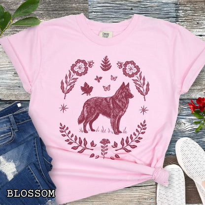 Pink Comfort Colors t-shirt for Belgian Sheepdog/Tervuren lovers, with folk art design of Belgian Shepherd surrounded by botanical elements, done in linocut monochrome style. Shown on a wooden surface accompanied by jeans, shoes and accessories.