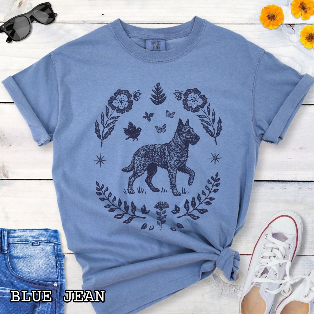 Blue Comfort Colors t-shirt for Belgian Laekenois lovers, with folk art design of Belgian Laekenois dog surrounded by botanical elements, done in linocut monochrome style. Shown on a wooden surface accompanied by jeans, shoes and accessories.