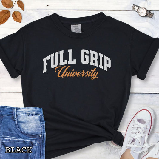 Black Comfort Colors t-shirt for bitework dog trainers with 'FULL GRIP University' text in college style lettering, shown on a wooden surface with jeans and sneakers.