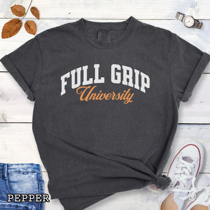 Dark grey Comfort Colors t-shirt for bitework dog trainers with 'FULL GRIP University' text in college style lettering, shown on a wooden surface with jeans and sneakers.