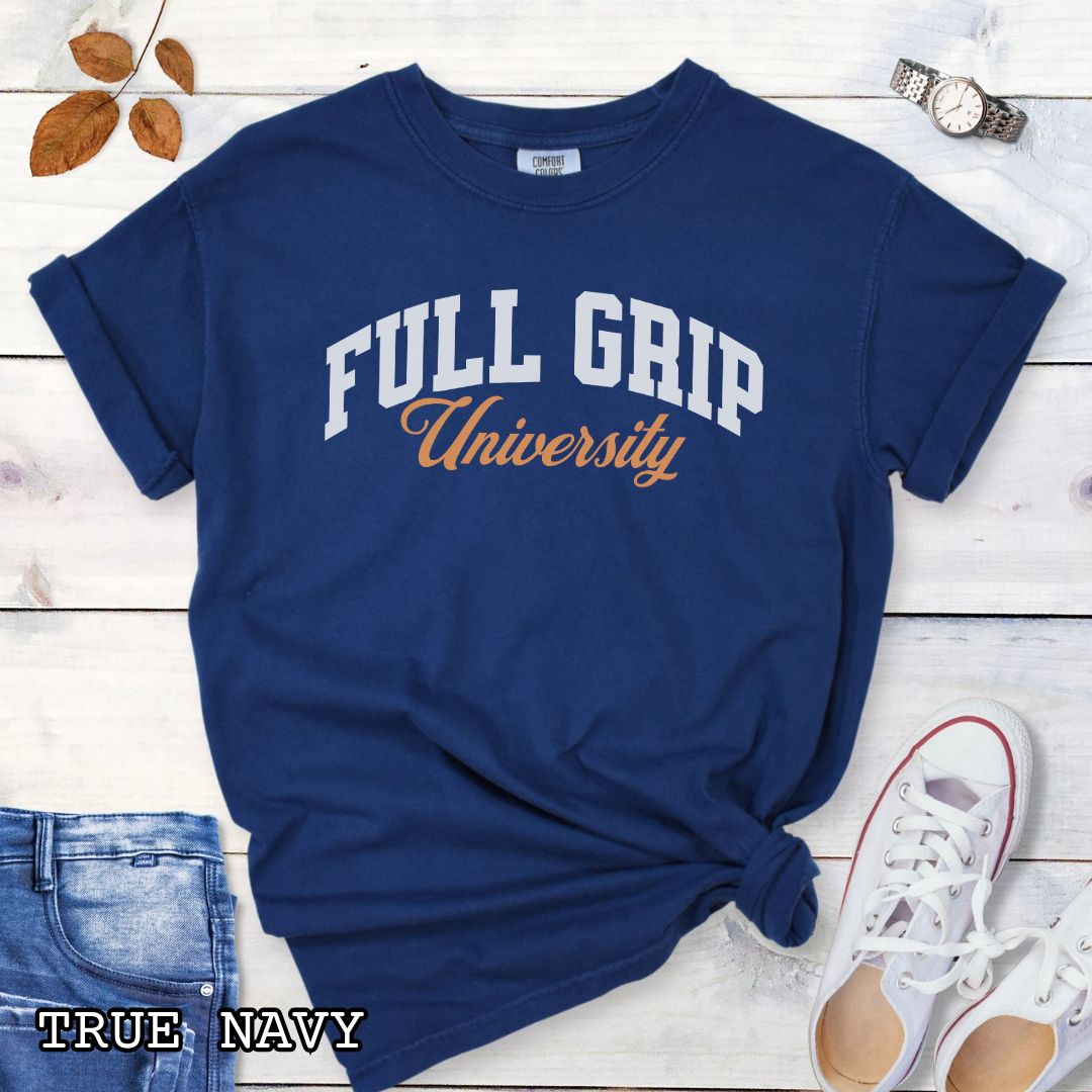 Navy blue Comfort Colors t-shirt for bitework dog trainers with 'FULL GRIP University' text in college style lettering, shown on a wooden surface with jeans and sneakers.