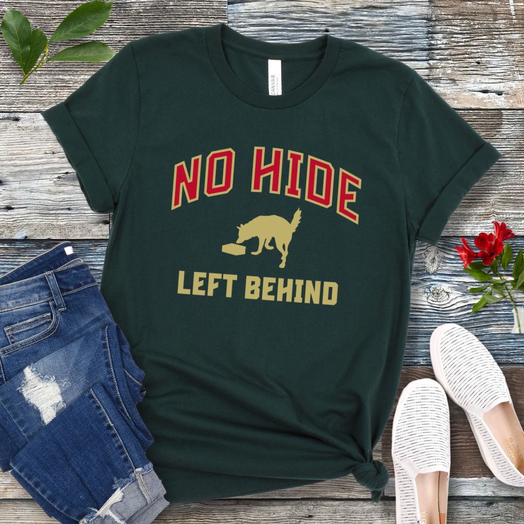 Forest green nosework t-shirt with 'No Hide Left Behind' text and sniffing dog graphic on a wooden surface with jeans and shoes.