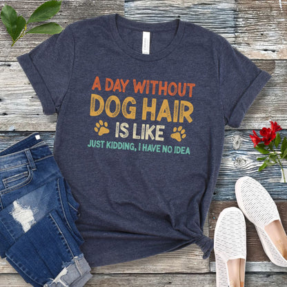 Heather navy t-shirt with colorful text 'A day without DOG HAIR is like, just kidding, I have no idea', presented on a wooden surface with jeans and casual shoes.