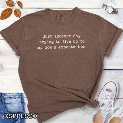 Brown Comfort Colors t-shirt featuring funny sarcastic 'Just Another Day Trying to Live Up to My Dog’s Expectations' quote, perfect humorous dog lover shirt for dog moms, dog dads, and pet parent gifts.