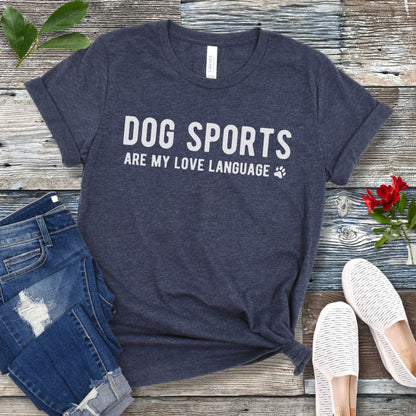 Heather navy t-shirt with 'Dog Sports are my love language' text on a wooden surface with jeans and shoes.