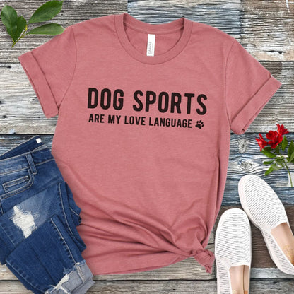 Mauve t-shirt with 'Dog Sports are my love language' text on a wooden surface with jeans and shoes.