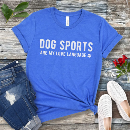 Royal blue t-shirt with 'Dog Sports are my love language' text on a wooden surface with jeans and shoes.