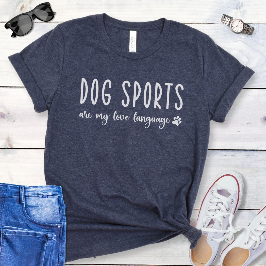 Heather navy dog training t-shirt with 'Dog Sports are my love language' text on a wooden surface with jeans and shoes.