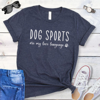Heather navy dog training t-shirt with 'Dog Sports are my love language' text on a wooden surface with jeans and shoes.