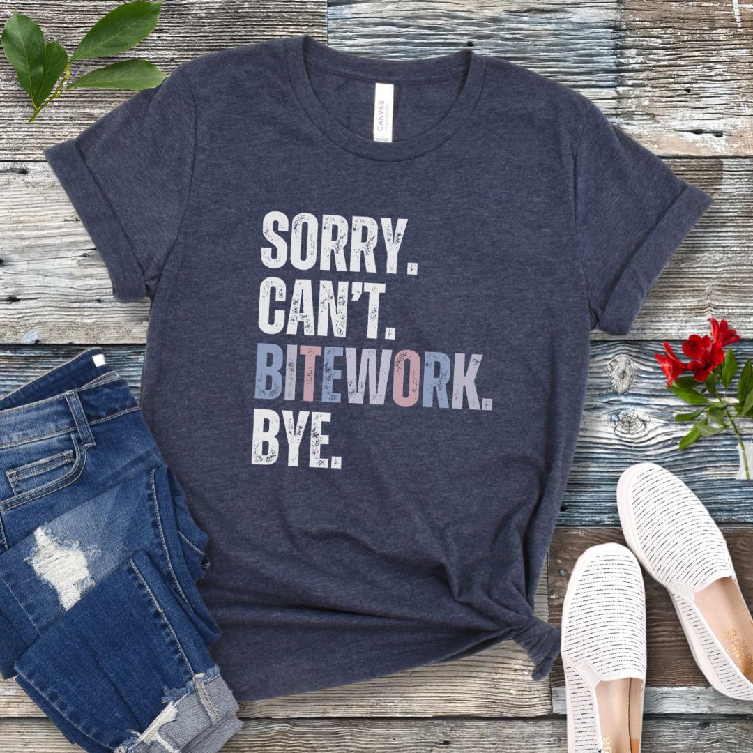 Heather navy protection dog training t-shirt with colorful, distressed text 'SORRY. CAN'T. BITEWORK. BYE.', presented on a wooden surface with jeans and shoes.