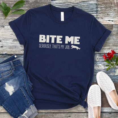 Navy blue bitework t-shirt with 'BITE ME Seriously, That's My Job' text and running dog graphic, presented on a wooden surface with jeans and shoes.