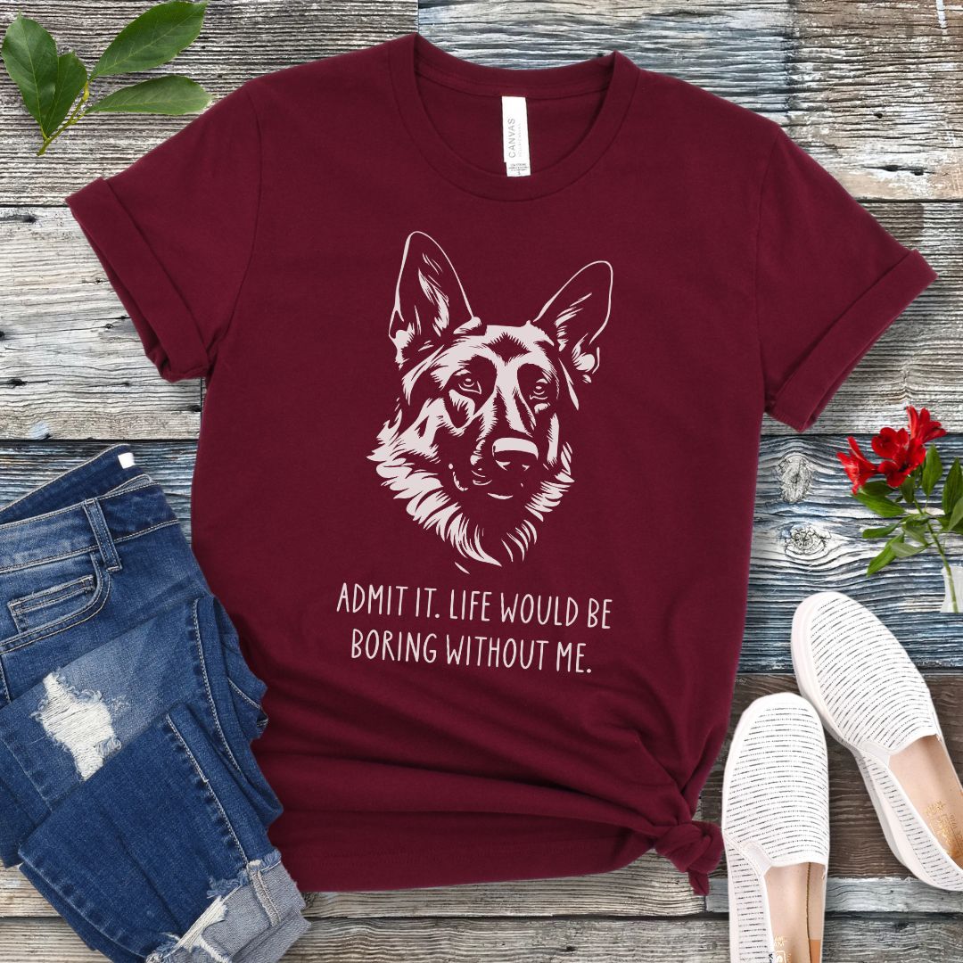 Maroon t-shirt for German Shepherd lovers with with Shepherd dog face graphic and humorous text 'Admit it. Life would be boring without me'. Shown on a wooden surface with accessories.
