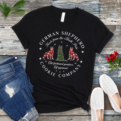 Black t-shirt with German Shepherd-shaped Christmas cookies and text  'German Shepherd Cookie Company', presented on a wooden surface with jeans and shoes.